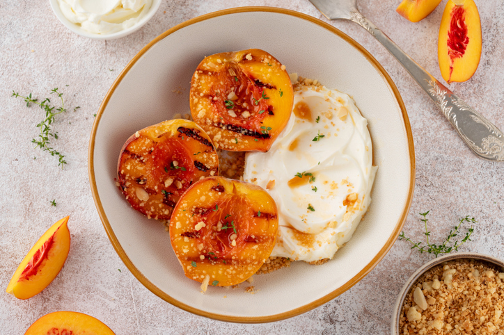 Delicious grilled peaches with mascarpone cream, honey syrup, crumbs and thyme in a bowl on a concrete background. Summer dessert. Top view.